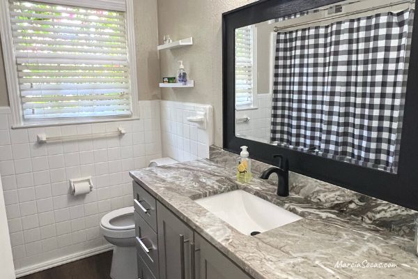 renovated bathroom showing gray cabinet, granite counters, new mirror, checkered shower cutain, in Alabama Airbnb