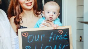 woman carrying a baby holding a small blackboard